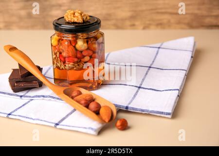 Different nuts with honey in jar, spoon and chocolate on beige