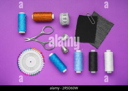 Flat lay composition with thimbles and different sewing tools on purple background Stock Photo