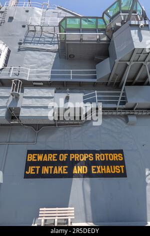 The island of the USS Yorktown has a warning sign saying, 'Beware of Props Rotors Jet Intake and Exhaust.' Stock Photo