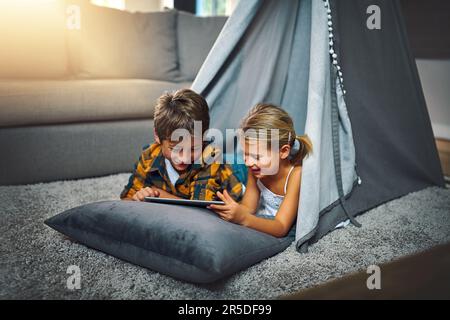 They sure do enjoy the wifi at home. an adorable little boy and girl using a tablet together while chilling in a homemade tent in the living room at Stock Photo