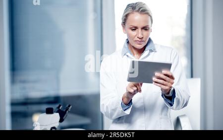 Processing scientific data on her device. a mature scientist using a digital tablet while working in her lab. Stock Photo