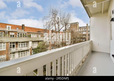 a balcony with white railings and brick buildings in the background, there is a tree on the right side Stock Photo