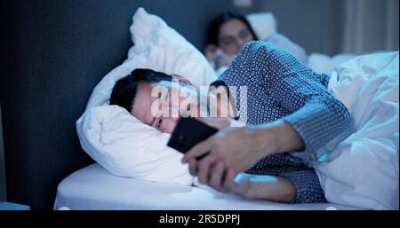 Young Man Using Cellphone While Her Wife Sitting On Bed At Night Stock Photo