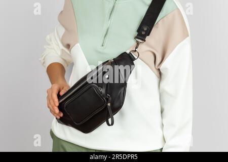 Close up Photo of the Black Genuine Leather Banana Bag with Zipped Pocket Wearing Crossbody on the Female Model over Grey Background Stock Photo