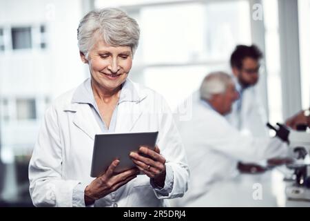 Sharing ideas with fellow doctors. a cheerful elderly female scientist using a digital tablet while standing inside of a laboratory. Stock Photo