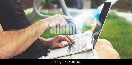 Man working on laptop in garden. Close-up of male hands typing Stock Photo