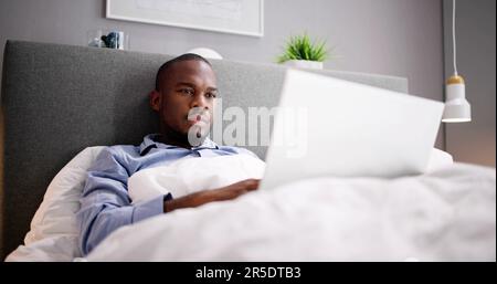 Happy Man Sitting On Bed Using Laptop Stock Photo