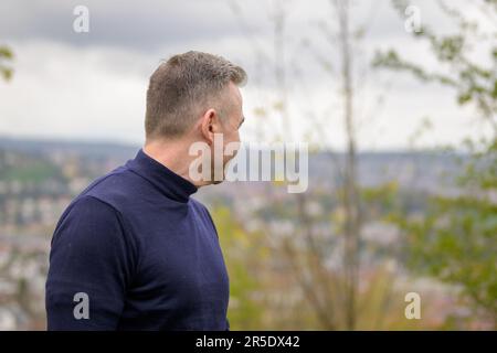 Middle age grey-haired attractive man wearing a blue sweater stands on a mountain and looking behind Stock Photo