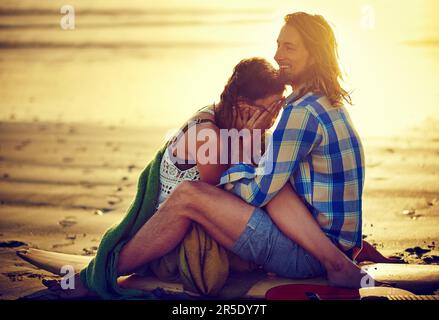 Stop it, youre making me shy. a couple sitting on the beach with their legs intertwined. Stock Photo