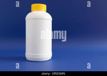 Pipe Unclogging Granules In Yellow Cap, White Plastic Bottle On Blue Purple Background. Acid Drain Cleaner, Housework Help. Horizontal Plane, Copy Stock Photo