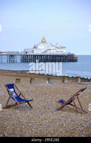 Two empty deckchairs facing each other on desserted shingle beach with pier in background Stock Photo