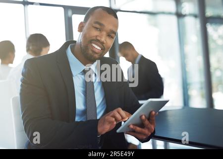 Its great for making notes during our meetings. Portrait of a happy young businessman using a digital tablet during a meeting at work. Stock Photo