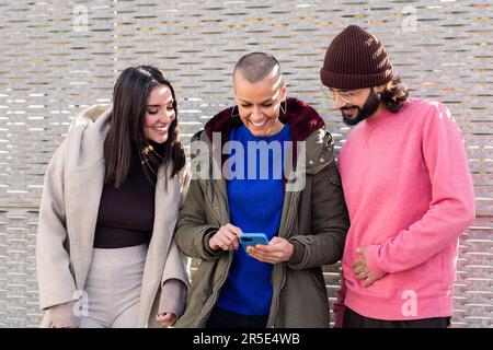 three smiling young friends enjoying using phone Stock Photo