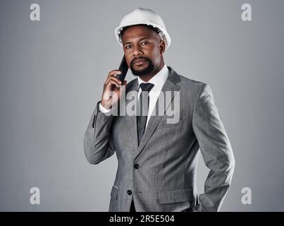 He works as hard as his team. Portrait of a well-dressed civil engineer using his cellphone while standing in the studio. Stock Photo