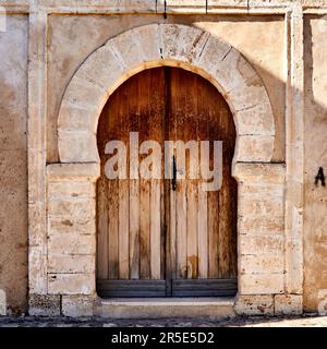 Sousse, Tunisia, January 22, 2023: Weathered massive antique wooden door in a stone arch in the ancient wall of the old town, medina, of Sousse Stock Photo