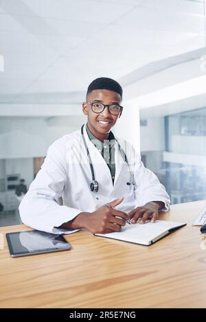 Is that all. a handsome young doctor sitting alone in his office at the clinic and using his notebook. Stock Photo