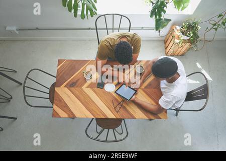 Going over our business plan. High angle shot of two unrecognizable friends sitting together and using a tablet in a coffeeshop. Stock Photo