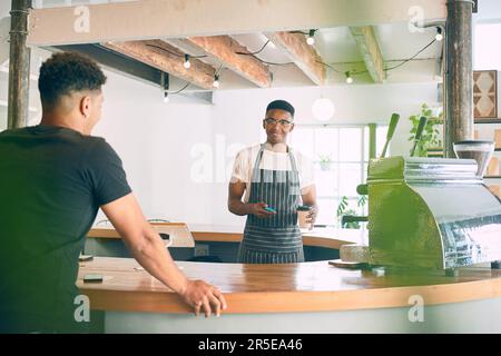 Satisfied customers keep coming back. a young man being served coffee in a cafe. Stock Photo