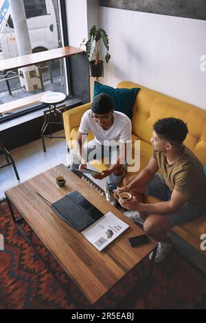Were so close to getting our business up and running. two men using a laptop and a digital tablet while having coffee together. Stock Photo