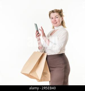 Woman buyer holds smartphone in hand and orders in an online shopping store. Satisfied caucasian ethnicity female 49 years old dressed in white blouse Stock Photo