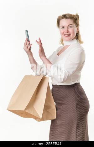 Happy female shopper holding shopping bags and using mobile phone app buy clothes online in e-commerce digital store. 49 years old woman Stock Photo