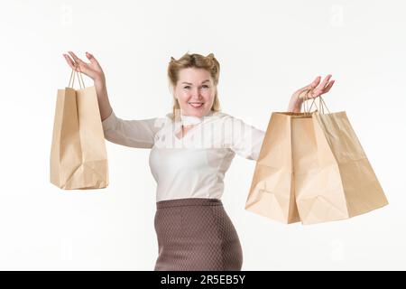 Waist up photo of happy smiling blonde woman holding shopping paper disposable bags with purchases. Female model 49 years old dressed in white blouse Stock Photo