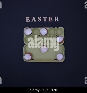 Egg shells arranged in an egg box on a black background with the inscription Easter. Minimalistic life style scene. Stock Photo