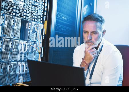 I hope there isnt a virus on this system. a mature man looking thoughtful while using a laptop in a server room. Stock Photo