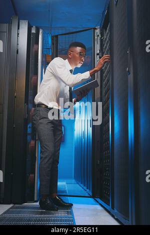 Making sure my system is still running smoothly. Full length shot of a young IT specialist standing alone in the server room and using a digital Stock Photo