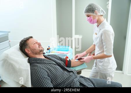 Specialist in a medical uniform takes blood from middle-aged patient Stock Photo