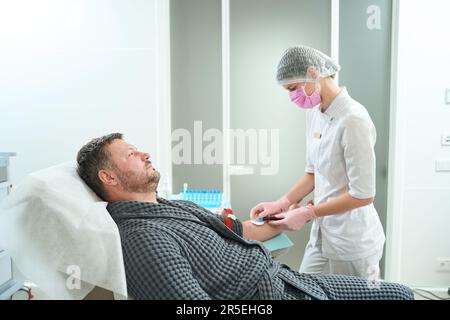 Woman in a medical uniform takes blood from a patient Stock Photo