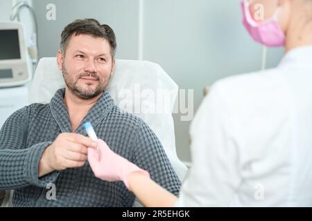 Male takes container for collecting biological material from health worker Stock Photo