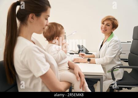 Joyous pediatric doctor receiving woman with infant in her office Stock Photo