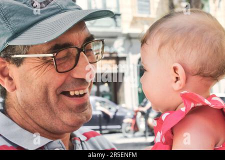Close-up headshot of a white Caucasian mature father / grandfather playing with a cute baby girl toddler and smiling Stock Photo