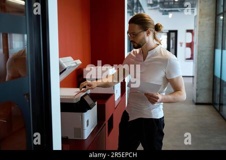 Handsome male worker using multifunction printer indoors Stock Photo