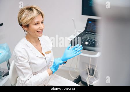 Joyful woman gynecologist wearing medical gloves before examining patient Stock Photo