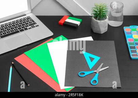 Paper sheets in colors of UAE flag with stationery on table near light wall Stock Photo