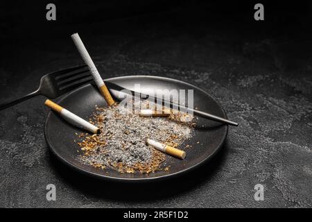 Plate with cigarettes, ash and cutlery on dark background. Stop smoking  concept Stock Photo