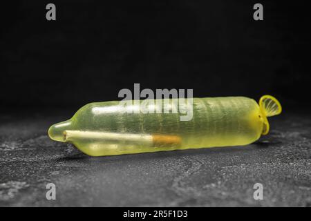 cigarette condom Inflated condom with cigarette inside on dark background. Stop smoking  concept Stock Photo