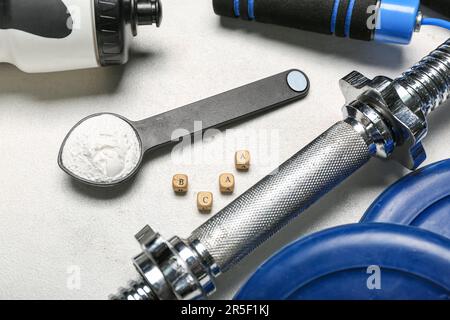 Scoop with amino acid supplement and sports equipment on light background, closeup Stock Photo