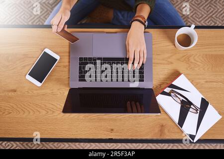 This is what I call convenience. High angle shot of an unrecognizable woman using a laptop and credit card to do some online shopping at home. Stock Photo