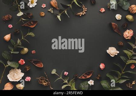 Autumnal-winter concept with dried flowers, branches of eucalyptus, leaves and berries on dark background. Frame of plants. Flat lay, copy space. Stock Photo