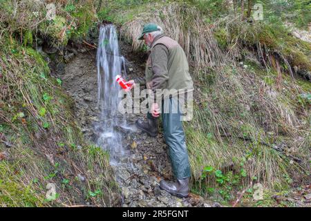 Crystal clear thirst quencher for outdoor activities. A hiker fills up his drinking bottle with the finest, crystal-clear mountain water. Stock Photo