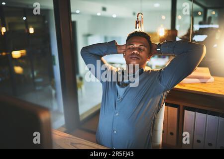 Feeling relaxed now that the work is done. a handsome young businessman looking relaxed while working late at night in a modern office. Stock Photo