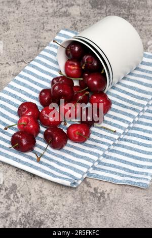 Fresh cherries spilled on kitchen towel and isolated on concrete background. Stock Photo