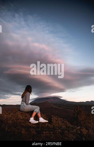 Girl sitting watching the lenticular clouds of the teide volcano at sunset in tenerife during her trip through the canary islands Stock Photo