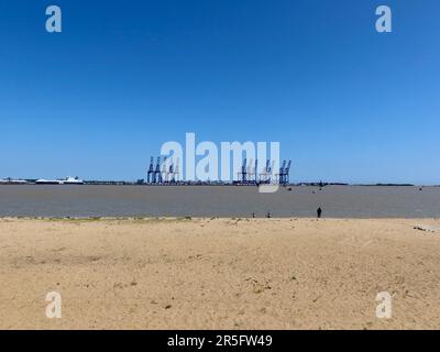 Harwich, Essex - 3 June 2023 : View from,the sandy beach across the harbour to the Port of Felixstowe cranes. Bright sunny afternoon and blue sky. Stock Photo