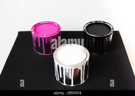 Three paint cans of white, pink and black paint form a triangle on a black background against a white background. Stock Photo