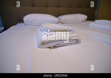 Clean white bath towels on the neatly clean bed of hotel room - coziness and clean concept. Stock Photo