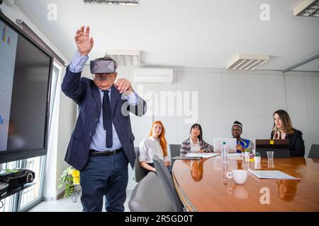 During a conference a businessman uses virtual reality headsets while others observe him Stock Photo